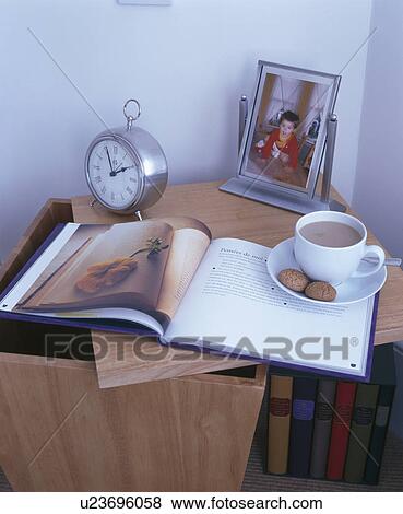 Stock Photo - Close-up of cup of tea on book beside alarm clock. Fotosearch