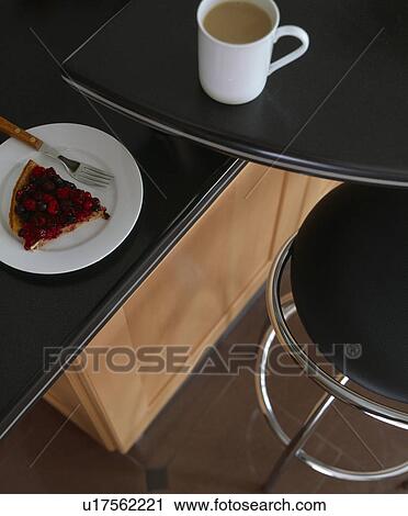 Stock Image - Close-up of cup of tea with cake on black granite worktop. Fotosearch