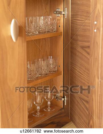 Stock Image - Close-up of cut-glass crystal glasses on shelves in fitted kitchen cupboard. Fotosearch