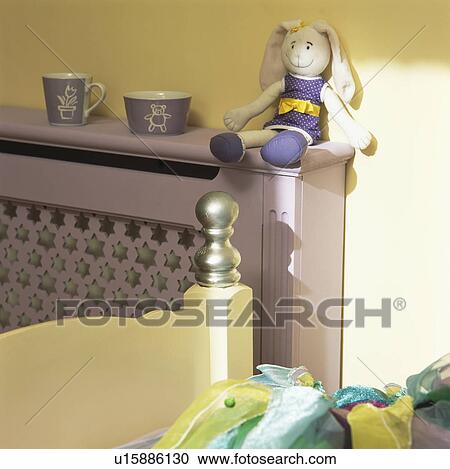 Stock Image - Close-up of doll on mauve fretwork radiator cover. Fotosearch