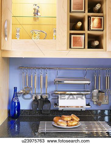 Stock Image - Close-up of doughnuts on plate below metal storage rack. Fotosearch