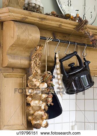 Stock Image - Close-up of enamel kettle and string of garlic on hooks hanging from pine shelf. Fotosearch