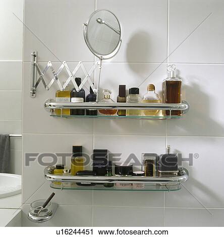 Stock Image - Close-up of extendable mirror above toiletry bottles on glass and chrome shelves. Fotosearch