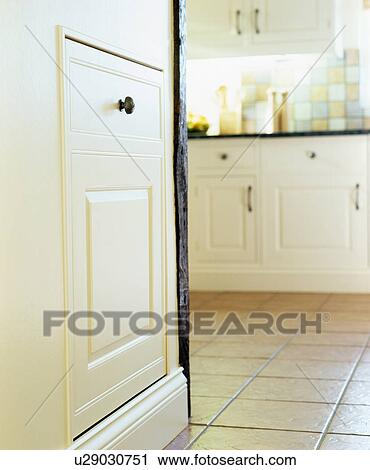 Stock Image - Close-up of fitted cupboard door concealing refrigerator in cream country kitchen with cream tiled floor. Fotosearch