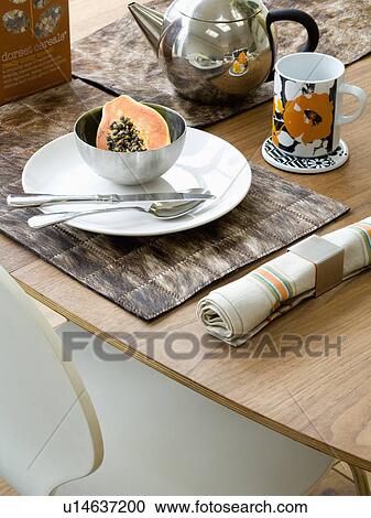 Stock Image - Close-up of fruit in bowl on white plate on table set for breakfast. Fotosearch