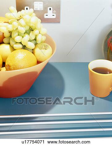 Stock Image - Close-up of fruit in orange plastic bowl on blue worktop. Fotosearch