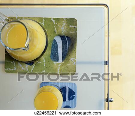 Stock Image - Close-up of glass jug or orange juice on pebble-patterned glass tray. Fotosearch
