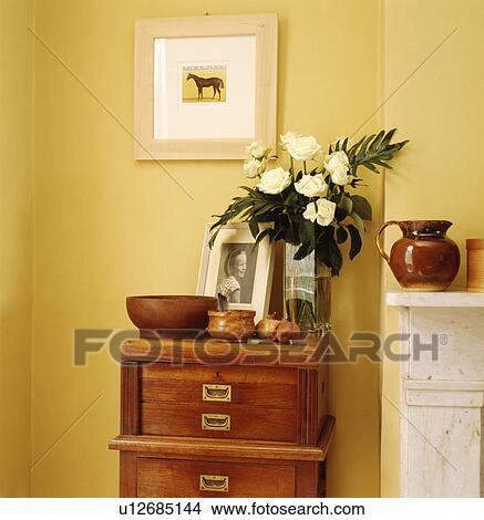 Picture - Close-up of glass vase of cream roses on chest-of-drawers. Fotosearch