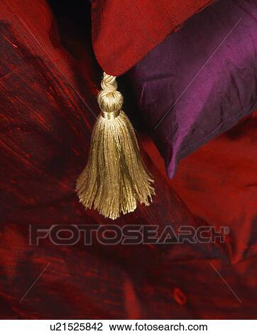Stock Image - Close-up of gold tassel and red silk cushions. Fotosearch