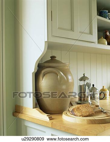 Stock Photo - Close-up of large earthenware crock and wooden chopping board on kitchen worktop. Fotosearch