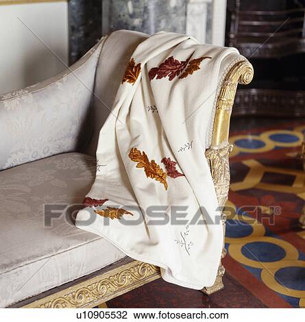 Stock Image - Close-up of leaf-embroidered throw on antique gilt sofa with grey silk upholstery. Fotosearch
