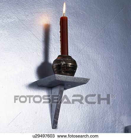 Stock Image - Close-up of lighted candle on small wall-shelf. Fotosearch