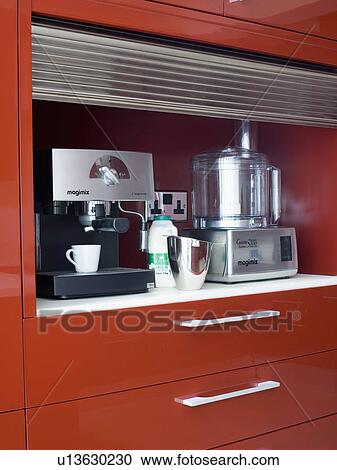 Stock Image - Close-up of Magimix coffee machine and food processor in storage cupboard with tambour shutter. Fotosearch