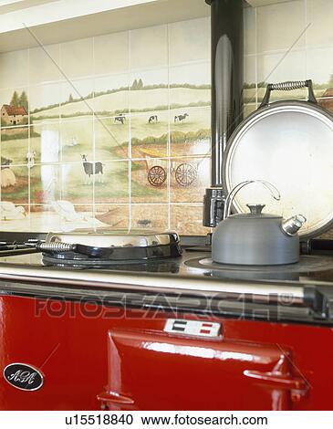 Stock Image - Close-up of metal kettle on red Aga oven. Fotosearch