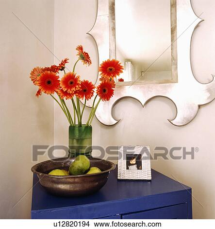 Close-up of metal mirror above vase of red gerberas on blue chest with bowl of green apples View Large Photo Image Picture - Close-up of metal mirror above vase of red gerberas on blue chest with bowl of green apples. Fotosearch