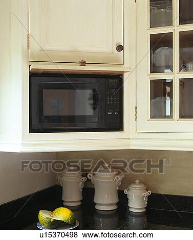 Stock Photo - Close-up of microwave oven in fitted cream cupboard with lift-up door. Fotosearch