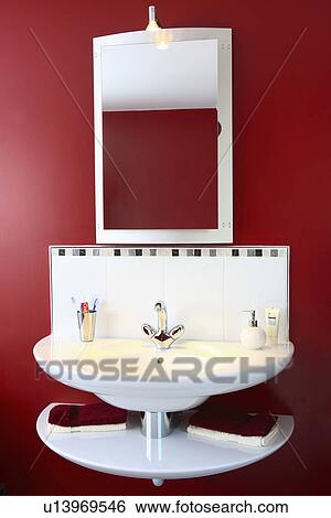 Stock Photograph - Close-up of mirror above modern white basin in red bathroom. Fotosearch