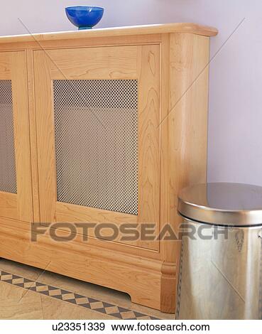 Stock Photo - Close-up of pale wood and metal mesh radiator cover and steel wastebin. Fotosearch