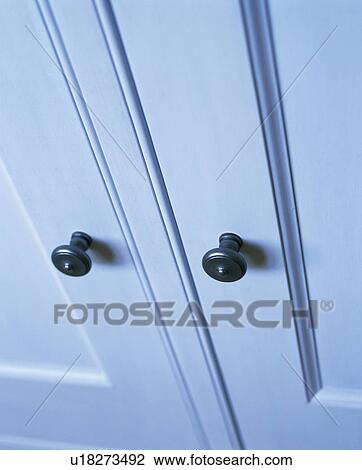 Stock Image - Close-up of pastel blue cupboard doors with black handles. Fotosearch