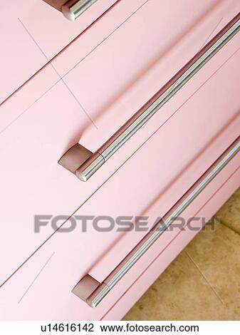 Stock Image - Close-up of pastel pink kitchen storage drawers with brushed-steel handles. Fotosearch