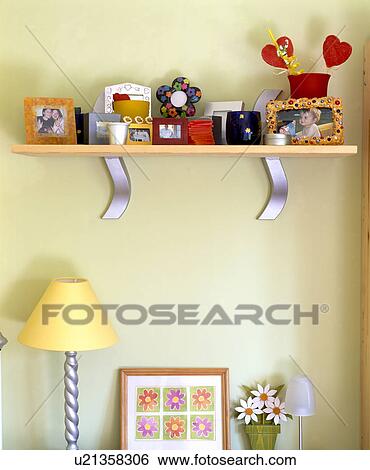 Stock Photograph - Close-up of photographs on wood and metal shelf above yellow lamp and small floral picture. Fotosearch