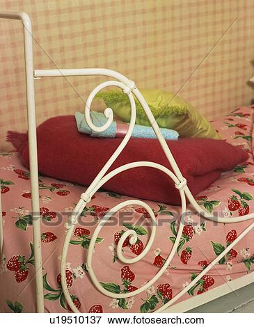 Stock Photo - Close-up of pink throw and rose-patterned quilt on white metal bed. Fotosearch