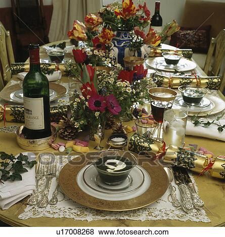 Stock Photo - Close-up of place settings and floral decorations on table set for Christmas lunch with gold paper crackers. Fotosearch