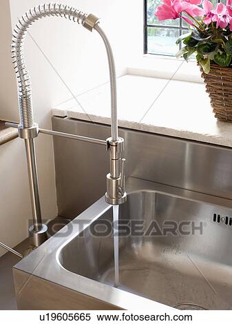 Stock Photography - Close-up of pull-out spray kitchen mixer tap pouring water into stainless steel sink. Fotosearch