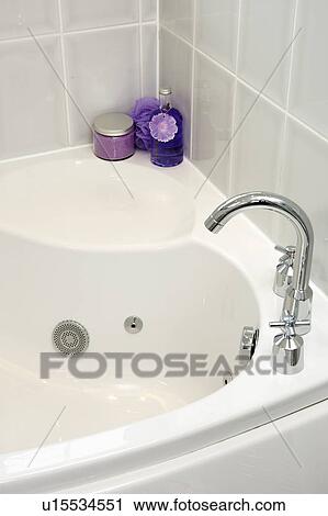 Stock Image - Close-up of purple bottles on corner of white bath with stainless steel tap. Fotosearch