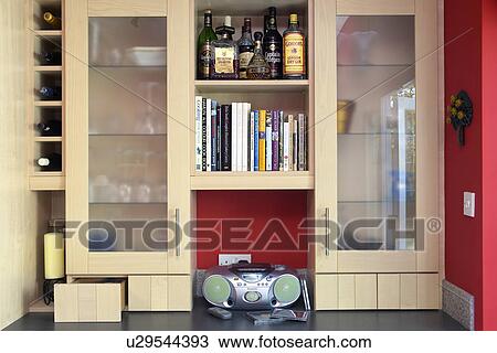 Stock Image - Close-up of radio below small shelves and glass-fronted kitchen cupboards. Fotosearch