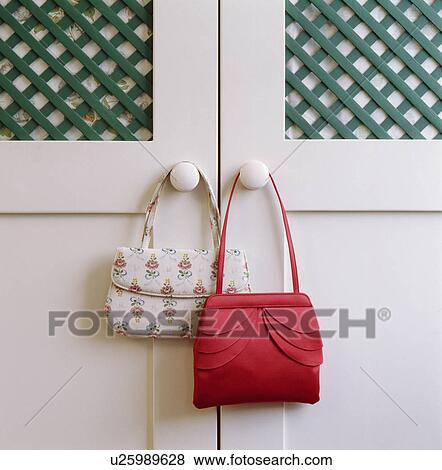 Stock Photo - Close-up of red silk handbag with floral handbag hanging on cupboard door. Fotosearch