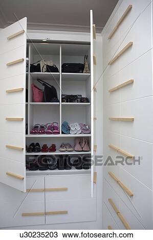 Stock Image - Close-up of shoes on shelves in fitted wardrobe with doors open. Fotosearch
