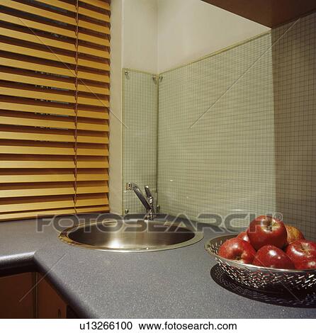 Stock Image - Close-up of sink in fitted unit below window with slatted wooden blind. Fotosearch