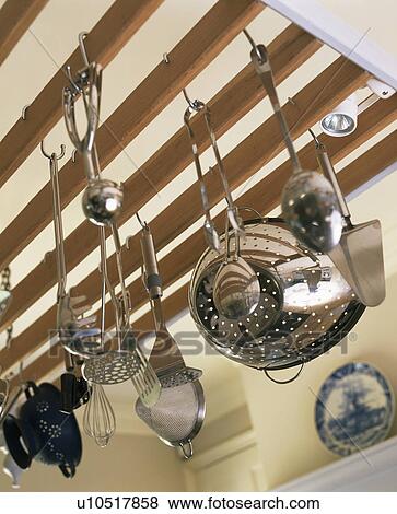 Stock Photo - Close-up of stainless-steel colander and utensils on wooden ceiling rack. Fotosearch