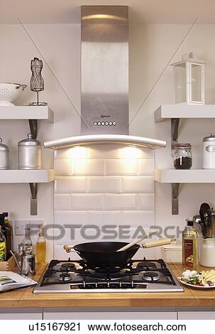 Stock Image - Close-up of stainless steel extractor with downlighting above wok on stainless steel gas hob. Fotosearch