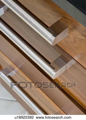Stock Image - Close-up of stainless steel handles on dark wood kitchen drawers. Fotosearch