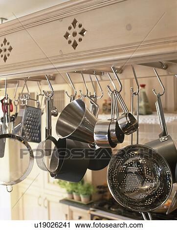 Stock Image - Close-up of stainless steel saucepans on hooks on cream hanging rack. Fotosearch