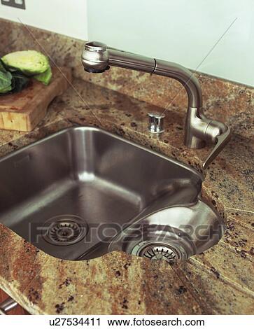 Stock Image - Close-up of stainless steel tap and sink in marble worktop. Fotosearch