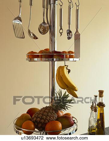Stock Image - Close-up of stainless steel utensils and fruit on circular steel storage shelves on steel pole. Fotosearch