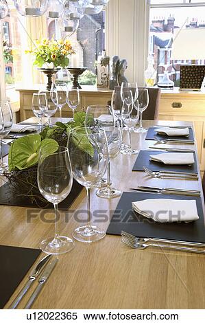 Stock Photography - Close-up of table set for lunch with white napkins and square black plates on pale wood table with wine glasses. Fotosearch