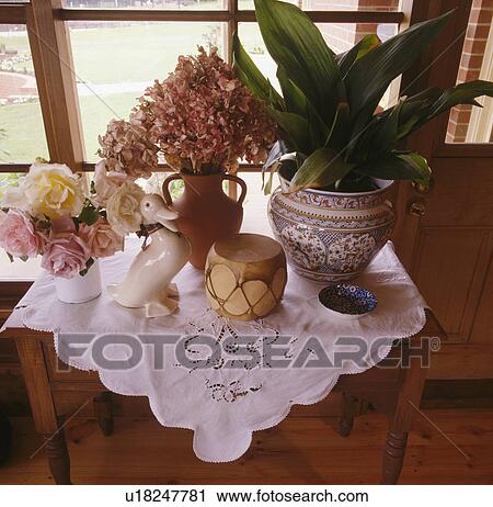 Stock Image - Close-up of table with broderie anglaise cloth and green houseplant in pot. Fotosearch