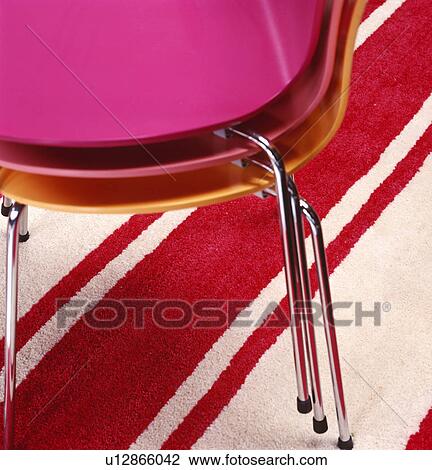Stock Image - Close-up of three modern pink chairs stacked on red+cream striped carpet. Fotosearch