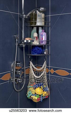 Stock Image - Close-up of toiletries and net bag of childre's plastic bath toys on steel shower shelves. Fotosearch