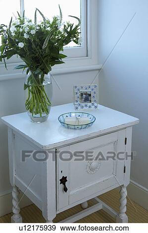 Stock Photo - Close-up of vase of flowers on small white painted cupboard. Fotosearch