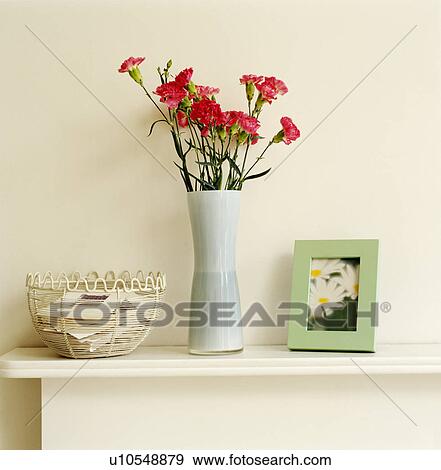 Stock Photo - Close-up of vase of red flowers on mantelpiece with small picture and cream wire basket. Fotosearch