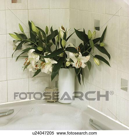 Stock Photography - Close-up of vase of white lilies on corner of bath. Fotosearch