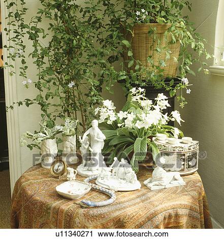 Stock Image - Close-up of white china ornaments on table with pots of white streptocarpus and white flowering jasmine. Fotosearch