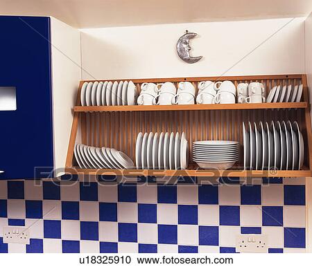 Stock Image - Close-up of white crockery on wooden plate-rack above blue+white ceramic tiles. Fotosearch