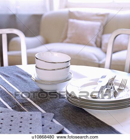 Stock Image - Close-up of white cups and plates on white table with blue striped runner. Fotosearch