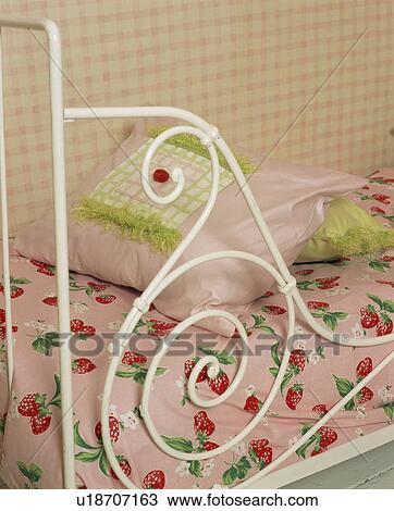 Stock Image - Close-up of white metal bed with pink cushion and strawberry-print bedlinen. Fotosearch